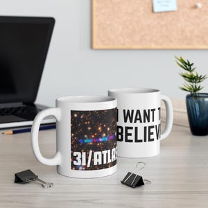 May include: Two white ceramic mugs. One mug features a starry space image with the text "31/ATLAS". The other mug has the text "I WANT TO BELIEVE" in black. Both mugs have a white handle.