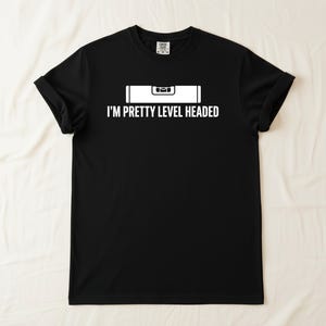 Puede incluir: Camiseta negra con el texto blanco "I'M PRETTY LEVEL HEADED" y un gráfico blanco de un nivel. La camiseta tiene mangas cortas y cuello redondo.