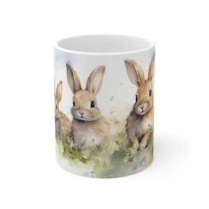 May include: White ceramic mug with a watercolor illustration of four brown rabbits in a grassy field. The rabbits are looking at the viewer.