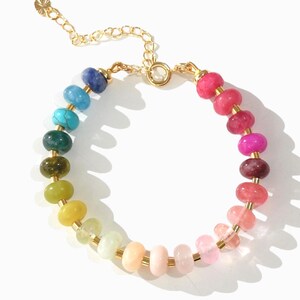 May include: A rainbow gemstone bracelet with a gold chain clasp. The bracelet features round beads in shades of blue, green, yellow, orange, pink, and red.