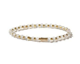 May include: A white beaded bracelet with gold accents. The bracelet is made of small, round beads and has a gold clasp.