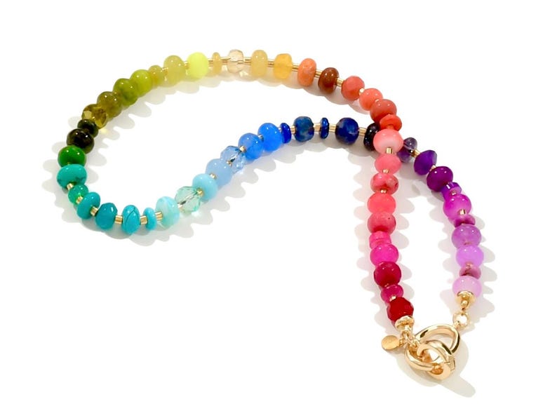 Colorful rainbow gemstone necklace featuring faceted natural stones in bold, vibrant hues with gold accents and a toggle clasp. Handmade statement jewelry displayed on a vanity with soft lighting, highlighting the sparkle and rich texture of each bead. Perfect for stacking or wearing solo.