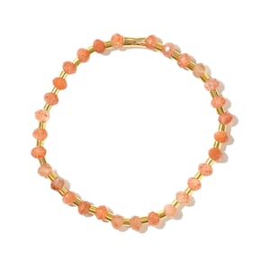 May include: A gold bracelet with small, orange-colored beads. The bracelet is made of metal and has a simple design.