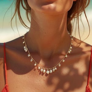 Delicate freshwater pearl necklace with gold chain and dangling pearl drops styled on sun-kissed skin at the beach with coastal resort-inspired aesthetic.