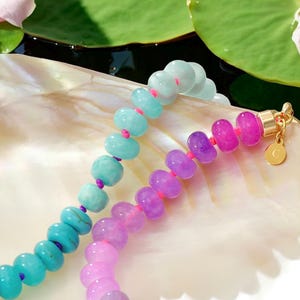 Hand-knotted gemstone necklace featuring turquoise, royal blue, and lilac beads with a gold clasp, laid out in a soft ombré gradient.
