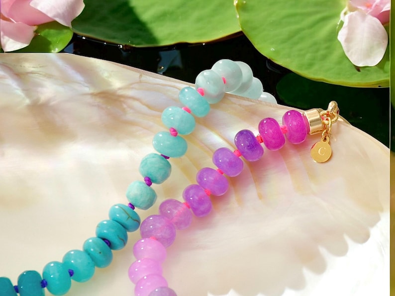 Hand-knotted gemstone necklace featuring turquoise, royal blue, and lilac beads with a gold clasp, laid out in a soft ombré gradient.