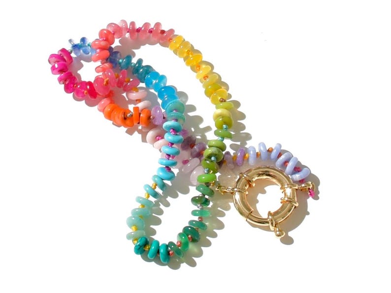 May include: A rainbow colored beaded necklace with a gold clasp. The beads are in a variety of shapes and sizes, and they are strung on a thin cord.