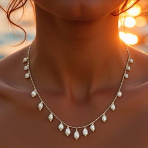Delicate freshwater pearl necklace with gold chain and dangling pearl drops styled on sun-kissed skin at the beach with coastal resort-inspired aesthetic.