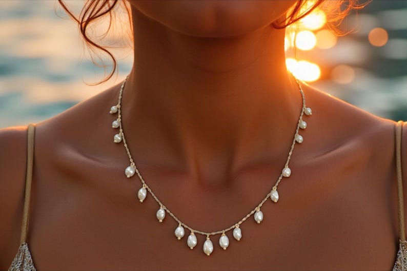 Delicate freshwater pearl necklace with gold chain and dangling pearl drops styled on sun-kissed skin at the beach with coastal resort-inspired aesthetic.