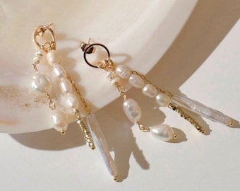May include: A pair of gold dangle earrings with white pearl accents. The earrings feature multiple strands of pearls and a long, thin pearl pendant.