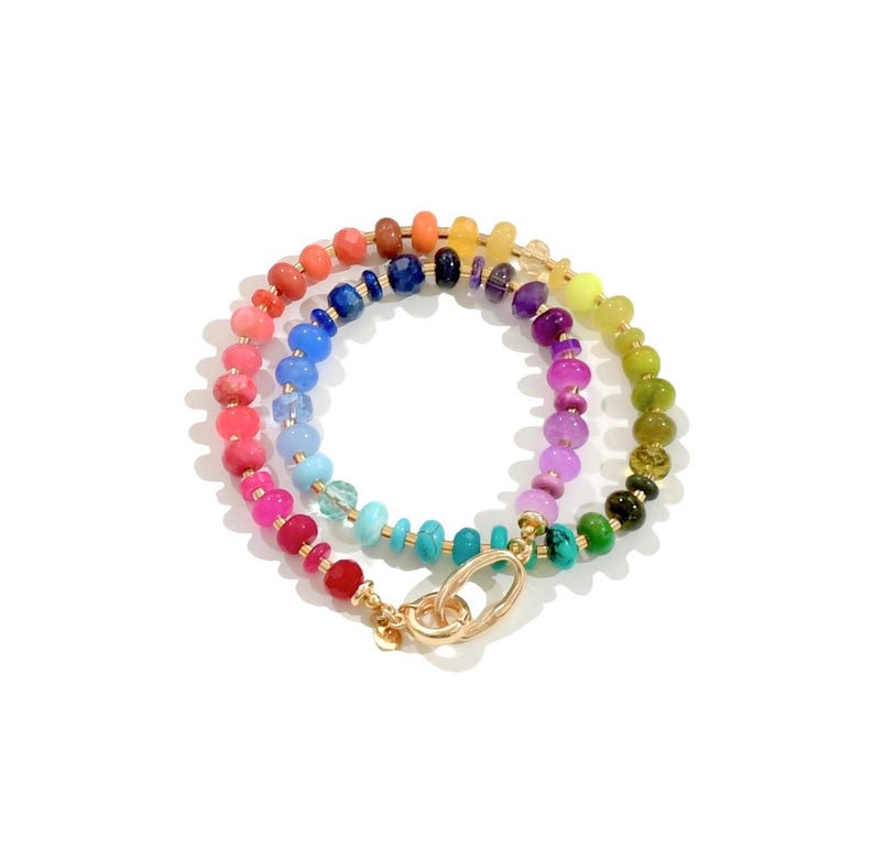 Colorful rainbow gemstone necklace featuring faceted natural stones in bold, vibrant hues with gold accents and a toggle clasp. Handmade statement jewelry displayed on a vanity with soft lighting, highlighting the sparkle and rich texture of each bead. Perfect for stacking or wearing solo.