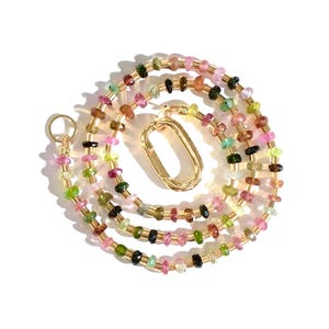 May include: A multi-colored gemstone necklace with a gold clasp. The necklace is made of small, faceted gemstones in shades of pink, green, and black.