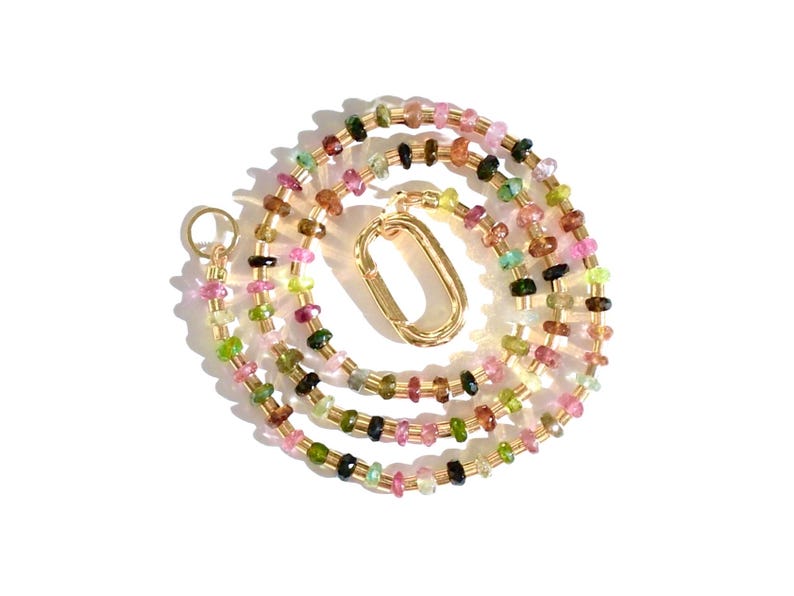 May include: A multi-colored gemstone necklace with a gold clasp. The necklace is made of small, faceted gemstones in shades of pink, green, and black.