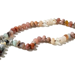 A long necklace made of various colored stones. The stones are in shades of brown, creams, white, and natural hues. The necklace has a gold clasp.