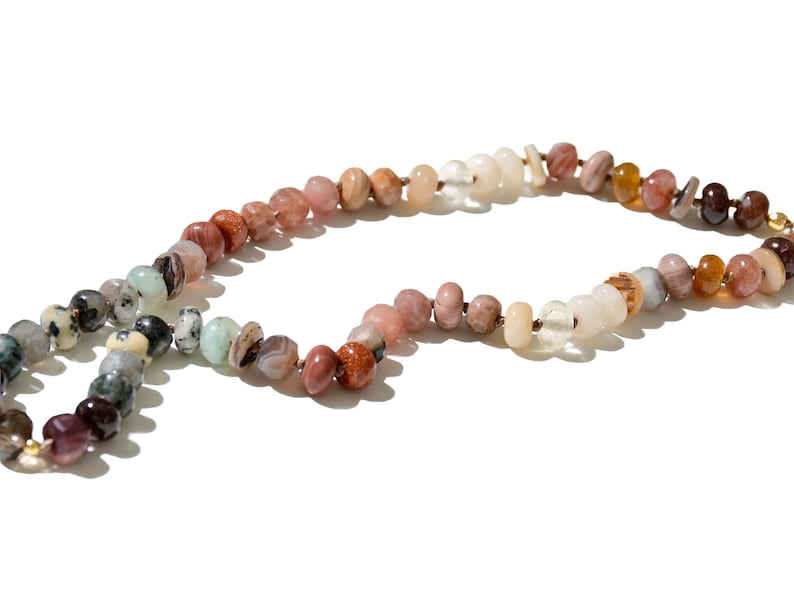 A long necklace made of various colored stones. The stones are in shades of brown, creams, white, and natural hues. The necklace has a gold clasp.