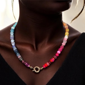 May include: A colorful beaded necklace with a gradient of blue, purple, pink, and red beads. The necklace has a gold clasp.