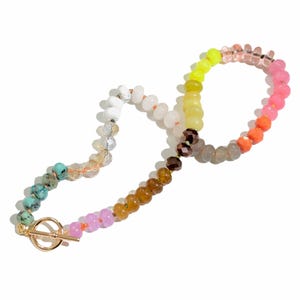 May include: A colorful beaded necklace with a gold toggle clasp. The beads are in shades of pink, orange, yellow, green, blue, and brown.