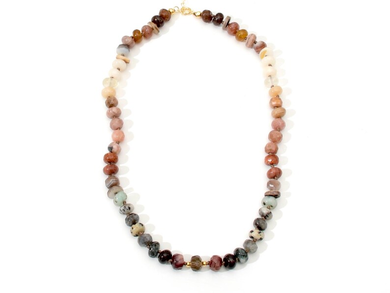 A long necklace made of various colored stones. The stones are round and have a natural, polished finish. The necklace is made of a gradient of colors, starting with light brown and transitioning to dark gray. The necklace is strung on a gold chain.
