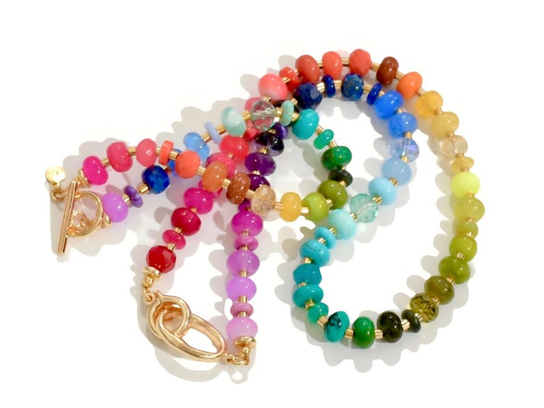 Colorful rainbow gemstone necklace and bracelet set featuring faceted natural stones in bold, vibrant hues with gold accents and a toggle clasp. Handmade statement jewelry displayed on a vanity with soft lighting, highlighting the sparkle and rich texture of each bead. Perfect for stacking or wearing solo.
