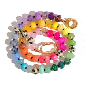 May include: A colorful beaded necklace with a rainbow of colors, including purple, yellow, pink, orange, green, and blue. The necklace has a gold clasp and a gold oval charm.