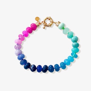 Gradient gemstone bracelet featuring genuine pink, lavender, cobalt blue, and aqua blue faceted beads with 14k gold vermeil accents and a gold toggle clasp on a white marble background.