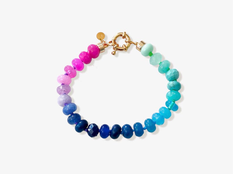 Gradient gemstone bracelet featuring genuine pink, lavender, cobalt blue, and aqua blue faceted beads with 14k gold vermeil accents and a gold toggle clasp on a white marble background.