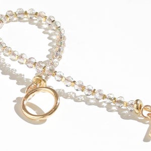 May include: A gold beaded bracelet with a clear crystal design. The bracelet has a gold toggle clasp and a gold ring.