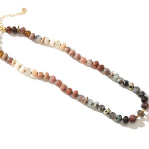 May include: A long necklace made of various colored stones. The stones are in shades of brown, creams, white, and natural hues. The necklace has a gold clasp.