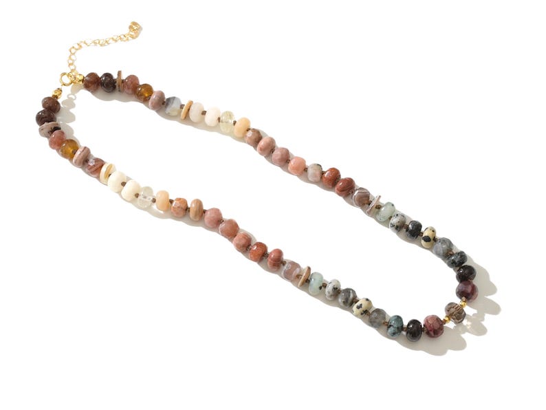 May include: A long necklace made of various colored stones. The stones are in shades of brown, creams, white, and natural hues. The necklace has a gold clasp.