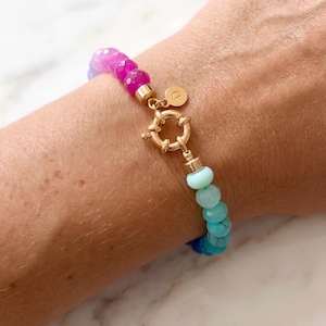 Gradient gemstone bracelet featuring genuine pink, lavender, cobalt blue, and aqua blue faceted beads with 14k gold vermeil accents and a gold toggle clasp on a woman’s wrist