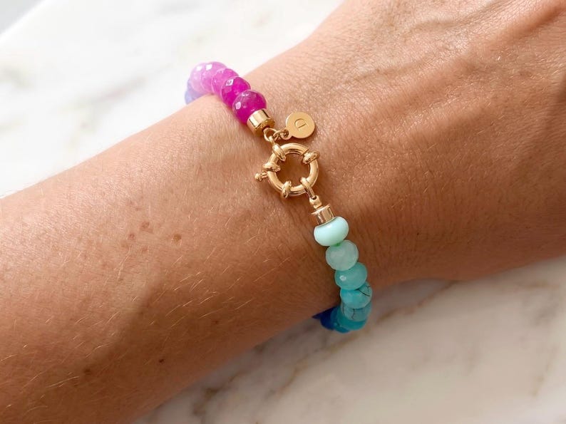 Gradient gemstone bracelet featuring genuine pink, lavender, cobalt blue, and aqua blue faceted beads with 14k gold vermeil accents and a gold toggle clasp on a woman’s wrist