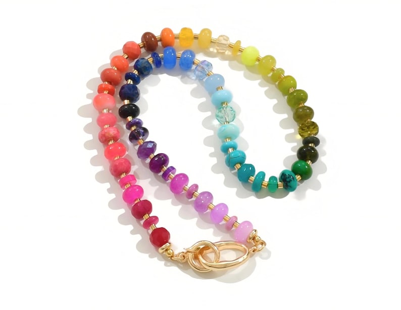 Colorful rainbow gemstone necklace featuring faceted natural stones in bold, vibrant hues with gold accents and a toggle clasp. Handmade statement jewelry displayed on a vanity with soft lighting, highlighting the sparkle and rich texture of each bead. Perfect for stacking or wearing solo.
