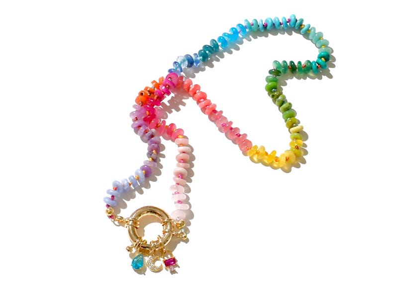 May include: A rainbow-colored beaded necklace with a gold clasp and charms. The beads are arranged in a gradient pattern, starting with blue and ending with yellow.