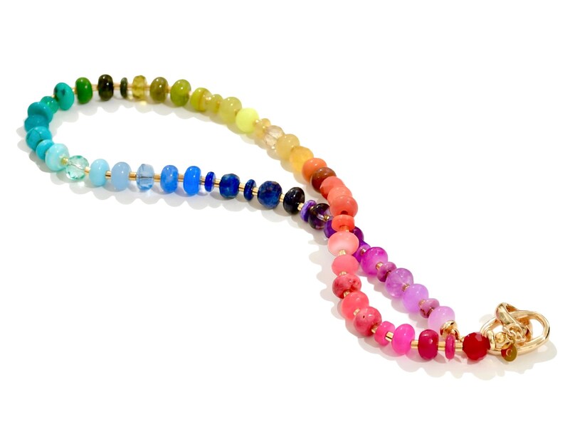 Colorful rainbow gemstone necklace featuring faceted natural stones in bold, vibrant hues with gold accents and a toggle clasp. Handmade statement jewelry displayed on a vanity with soft lighting, highlighting the sparkle and rich texture of each bead. Perfect for stacking or wearing solo.
