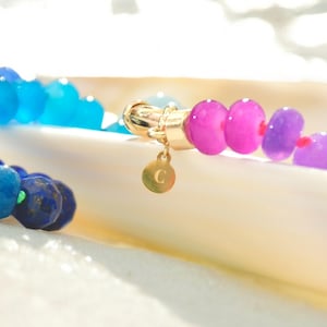 Hand-knotted gemstone necklace featuring turquoise, royal blue, and lilac beads with a gold clasp, laid out in a soft ombré gradient.