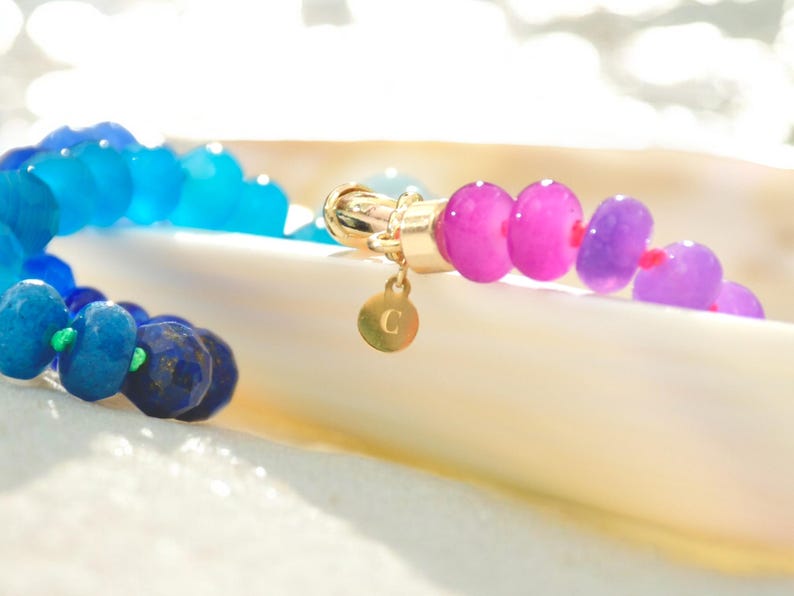 Hand-knotted gemstone necklace featuring turquoise, royal blue, and lilac beads with a gold clasp, laid out in a soft ombré gradient.