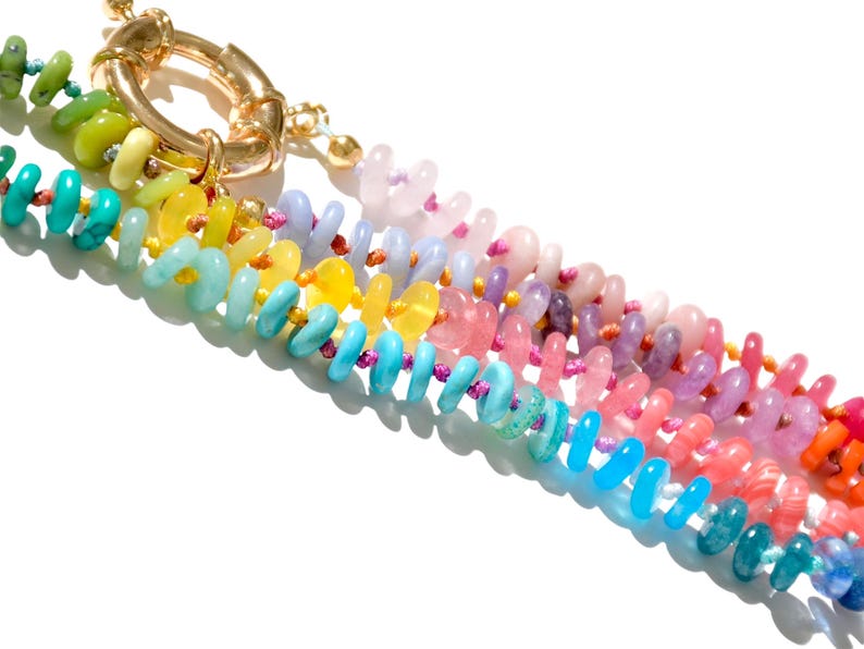May include: A multi-colored beaded necklace with a gold clasp. The beads are arranged in a rainbow pattern, with each color represented by a different type of stone.