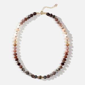 A long necklace made of various colored stones. The stones are in shades of brown, creams, white, and natural hues. The necklace has a gold clasp.