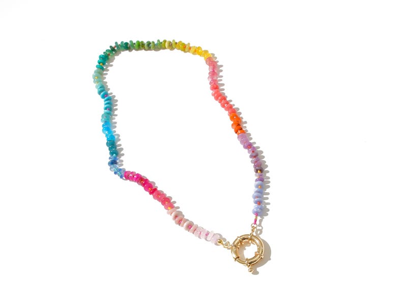 May include: A rainbow-colored beaded necklace with a gold clasp. The beads are small and round, and they are arranged in a gradient from green to purple.