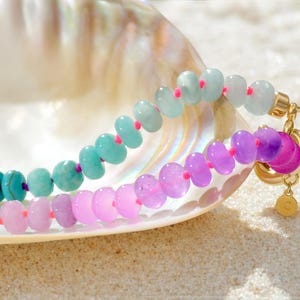Hand-knotted gemstone necklace featuring turquoise, royal blue, and lilac beads with a gold clasp, laid out in a soft ombré gradient.