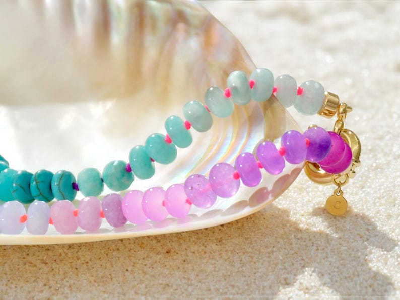 Hand-knotted gemstone necklace featuring turquoise, royal blue, and lilac beads with a gold clasp, laid out in a soft ombré gradient.