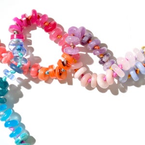 May include: A colorful beaded necklace with pink, purple, orange, blue, and green beads. The beads are strung on a thin cord and are arranged in a rainbow pattern.