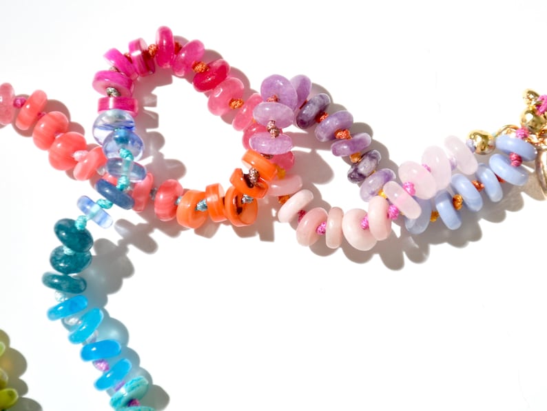 May include: A colorful beaded necklace with pink, purple, orange, blue, and green beads. The beads are strung on a thin cord and are arranged in a rainbow pattern.