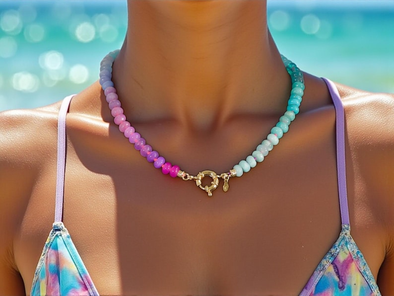 Hand-knotted gemstone necklace featuring turquoise, royal blue, and lilac beads with a gold clasp, laid out in a soft ombré gradient.