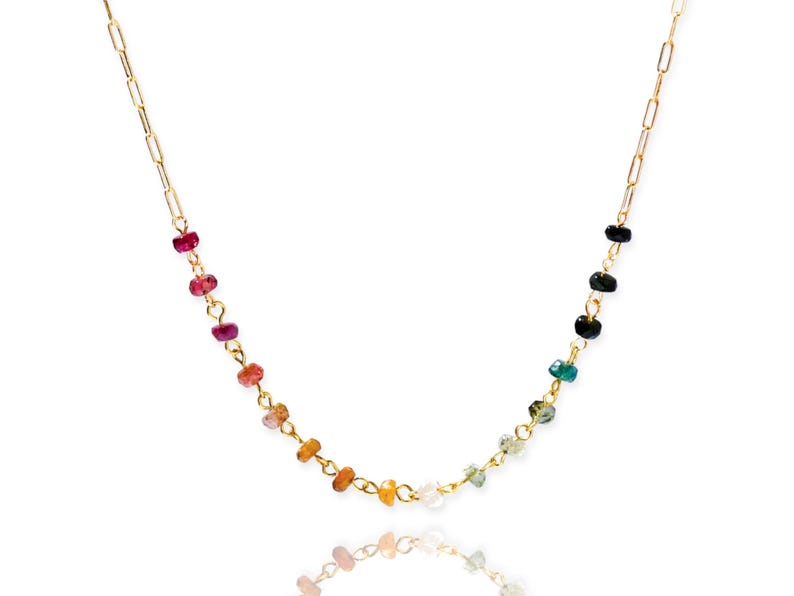 May include: A gold chain necklace with small, colorful gemstones. The gemstones are arranged in a rainbow pattern, with red, orange, yellow, green, blue, and purple stones.