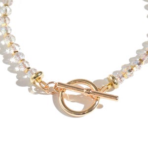 May include: A gold beaded necklace with a toggle clasp. The beads are clear and iridescent.