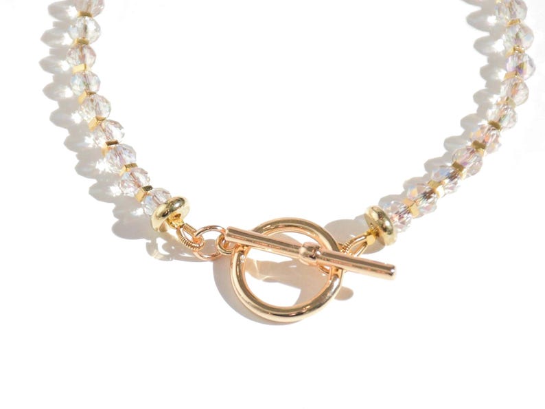 May include: A gold beaded necklace with a toggle clasp. The beads are clear and iridescent.