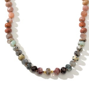 A long necklace made of various colored stones. The stones are in shades of brown, creams, white, and natural hues. The necklace has a gold clasp.