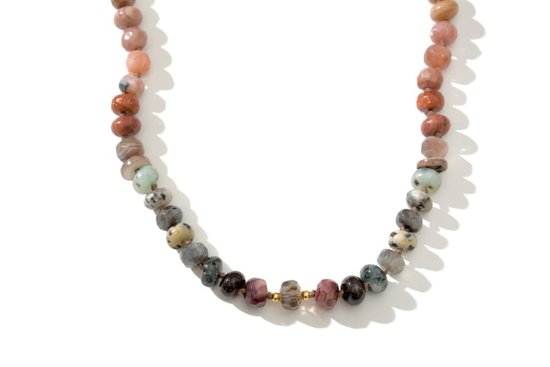 A long necklace made of various colored stones. The stones are in shades of brown, creams, white, and natural hues. The necklace has a gold clasp.