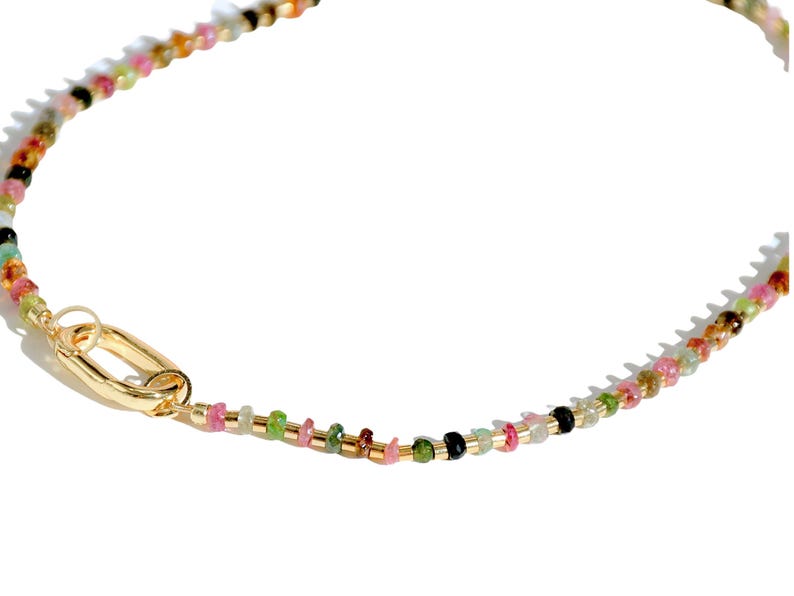 May include: A gold chain necklace with a multi-colored gemstone bead design. The necklace has a lobster clasp closure.